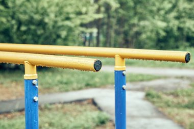 Sarı metal çubuklar, bulutlu bir günde baharda yeşil parktaki spor sahasında asılı duran yağmur damlalarıyla egzersiz yapmak için.