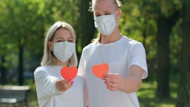 一个男人 一个穿着白色T恤 脸上戴着防护面具的女孩 用手将红心伸进镜框 连在一起 彼此凝视 安全的爱 — 图库视频影像