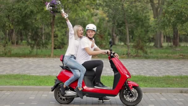 一个拿着一束花的女孩很高兴地把手举起来 坐在一辆红色的摩托车上 旁边坐着一个男人 — 图库视频影像
