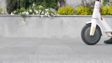 Yan görüntü, çerçeveye giren bir adam, yanında elektrikli bir scooter yuvarlıyor.. 