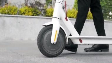 Takım elbiseli bir adam sokağın aşağısından yakın plan bir elektrikli scooter kullanıyor..