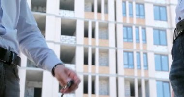 Yeni sahibi, emlakçıdan inşaat halindeki yeni evinin anahtarını alıyor ve el sıkışıyorlar, insanların bel seviyesini kapatıyorlar..