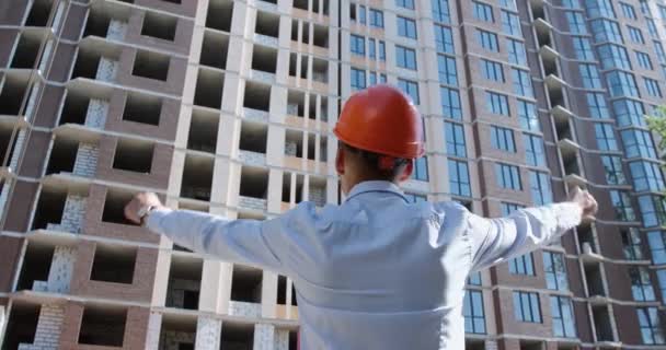 Человек Оранжевом Защитном Шлеме Стоящем Перед Строящимся Жилым Зданием Поднимает — стоковое видео