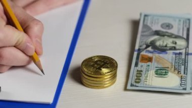 Bir dijital para tüccarı bitcoin oranının değerini kağıda yazar. Yakınlarda bitcoin paraları ve dolar banknotları vardır..