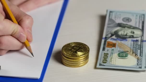 デジタル通貨トレーダーは紙にビットコインレートの値を書き込み ビットコインとドル紙幣が近くにあります — ストック動画