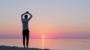 Ofis kıyafetleri içinde genç bir adam sabahın erken saatlerinde deniz kıyısında ısınıyor. Denizde tatilde olan bir ofis çalışanı