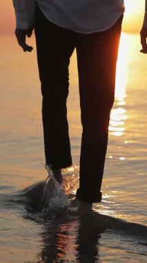 Sarılmış pantolonlu bir adam denize girer ve sırayla bacaklarını kaldırır. Güneşin arka planına su sıçratarak yaklaşır..