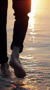 Bir adam deniz suyuna çıplak ayakla girer ve bacaklarını aniden sudan çıkararak sabah güneşine doğru bir püskürtme yapar..