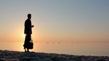 Elinde seyahat çantası olan takım elbiseli bir adam sakin bir denizin kıyısında duruyor ve sabah kahvesinden bir yudum alıyor. İşten sonra sınırsız özgürlük nefesi.