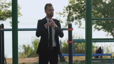 Takım elbiseli bir adam spor sahasında kollarını, başını ve omuzlarını yoğuruyor..