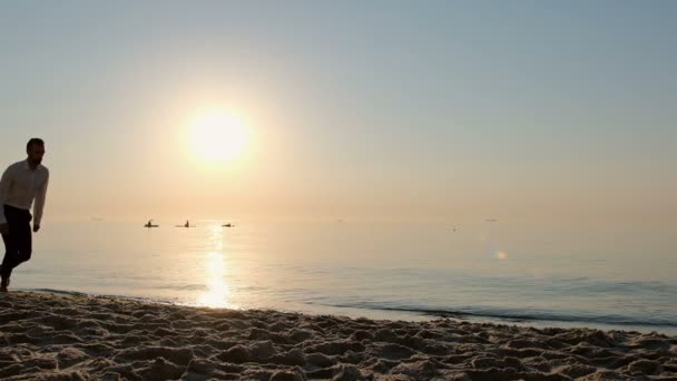 一个年轻人在沙滩上沿着沙滩跑着 在清晨的阳光映衬下在海面上跳跃着 慢动作120 Fps — 图库视频影像