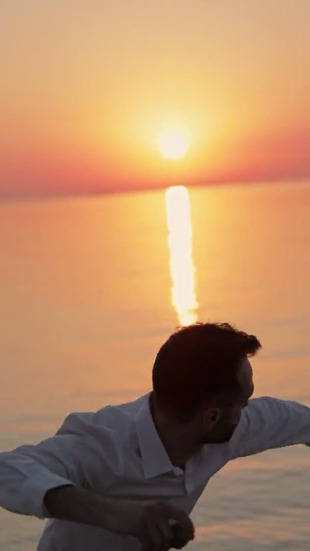 夜明けに海に面した男は 水の中に小さな石を投げた 垂直ビデオ — ストック動画