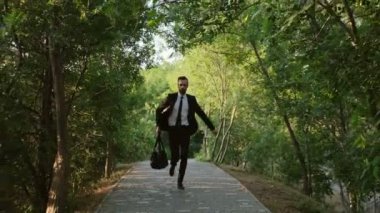 Takım elbiseli ve elinde çantasıyla bir işadamı yaz sabahının erken saatlerinde parkta hızla yürüyor..