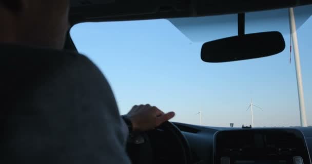 一名男子驾驶一辆电动汽车进入风电场的操作区域 车内司机肩膀后面的录像射击 — 图库视频影像