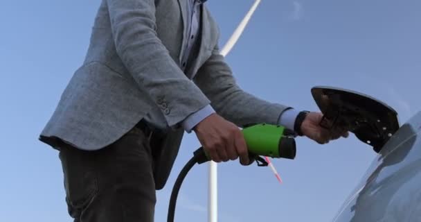 Hombre Conecta Cargador Coche Eléctrico Contra Fondo Las Palas Giratorias — Vídeos de Stock