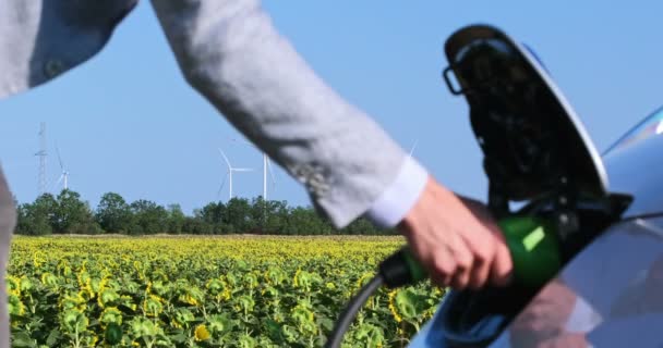 Man Connects Electric Car Charger Several Wind Generators Stop Background — Stock Video