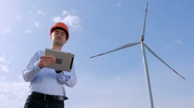 Koruyucu kasklı bir mühendis, yel değirmeni operasyonunu tablet kullanarak kontrol ediyor..
