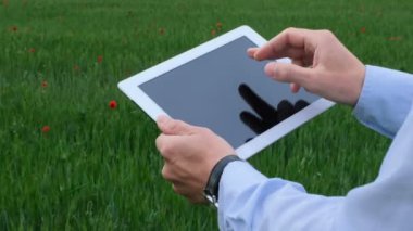 Bir mühendis yeşil alanda çalışan bir rüzgar jeneratörünün arka planına karşı tabletle çalışır. Rüzgar jeneratörü performans analizi.