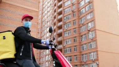 Sarı sırt çantalı, maskeli ve eldivenli bir teslimatçı elektrikli motosikletle videoda beliriyor ve baş parmağını kaldırıyor. Karantina sırasında mükemmel atış..