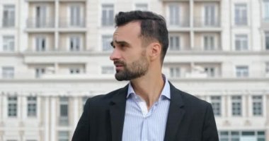 Takım elbiseli bir adam etrafına bakar ve bir telefona cevap verir, telefonda konuşur ve gülümser..