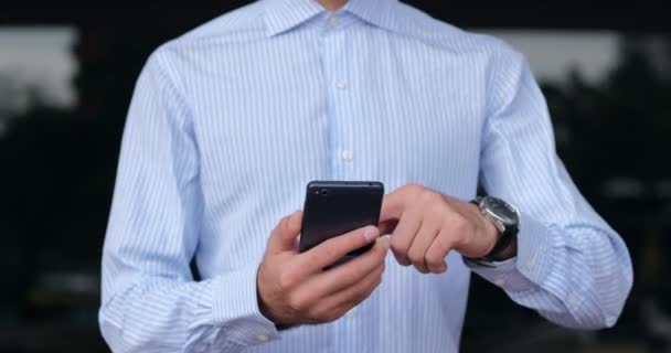 シャツを着た男が携帯電話を手に持ち 暗い窓の外ですぐに指を画面全体にスワイプします 高速5Gモバイルインターネット 顔のない中射 — ストック動画