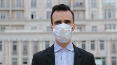 Takım elbiseli ve yüzünde tıbbi maske olan bir adam sokakta durup etrafa bakıyor. Karantina sırasında maskeli bir adam dışarıda duruyor..