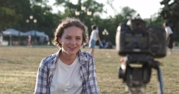Pozitivní žena blogger mluví s kamerou sedí na zeleném trávníku — Stock video