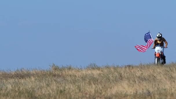 Žena s americkou vlajkou jezdí na kole na suché trávě pole — Stock video