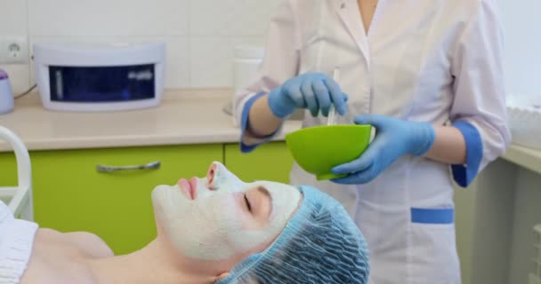 Frau mischt Maske auf Gesicht junger Klientin in Klinik auf — Stockvideo