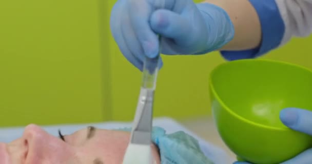 Kosmetolog nanáší na klientovu tvář na klinice hliněnou masku — Stock video