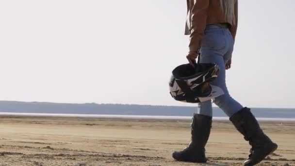 Mujer en chaqueta de cuero camina a lo largo de la playa de arena a moto — Vídeos de Stock