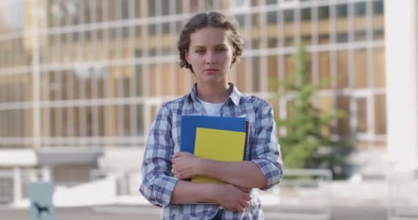 Estudiante en ropa casual sostiene cuadernos cerca de la universidad — Vídeos de Stock