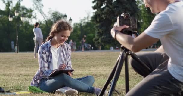 Видеограф снимает женщину, делающую домашнее задание на газоне — стоковое видео