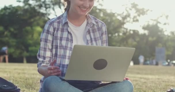 Κυρία με πουκάμισο χρησιμοποιεί βίντεο chat στο laptop κάθεται στο γκαζόν — Αρχείο Βίντεο