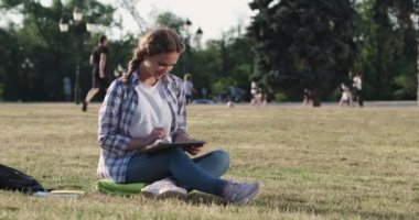 Neşeli kadın yeşil çimlere tablet çiziyor.