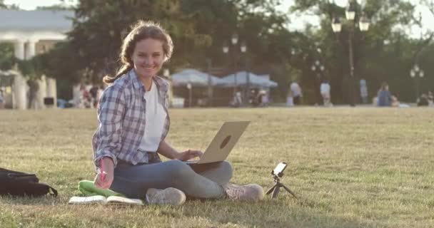 Estudiante feliz hace la tarea en el ordenador portátil sentado en la hierba — Vídeos de Stock