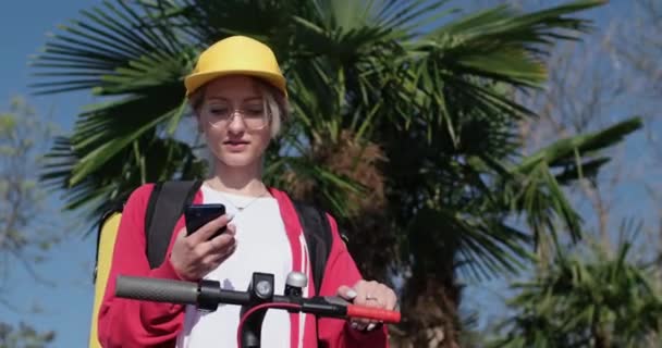 Señora trabajador de entrega en la tapa mira en orden en el teléfono inteligente — Vídeos de Stock