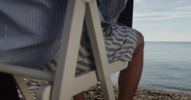 Mezítlábas üzletember ül fából készült széken a homokos tengerparton — Stock videók