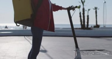 Elektronik scooter 'da büyük çantalı genç bir kadın esniyor.