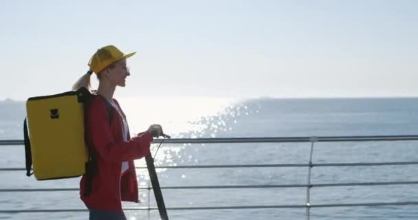 Mladá žena dodávka pracovník se žlutým sáčkem čepice na skútru — Stock video
