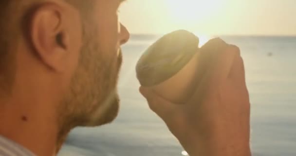 Biznesmen w garniturze pije kawę z papierowej filiżanki na brzegu morza — Wideo stockowe