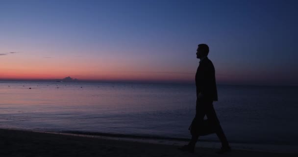 Uomo in abito classico passeggiate lungo la spiaggia sabbiosa tenendo borsa — Video Stock