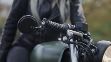 Sarışın, motosiklet gidonunda elini deri eldivene koyar.