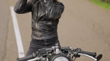 Siyah deri ceketli sarışın bayan motorcu miğfer takıyor.