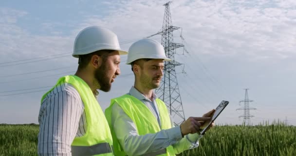 Mitarbeiter in Hardhats mit Tablet testen Stromleitungen auf dem Feld — Stockvideo