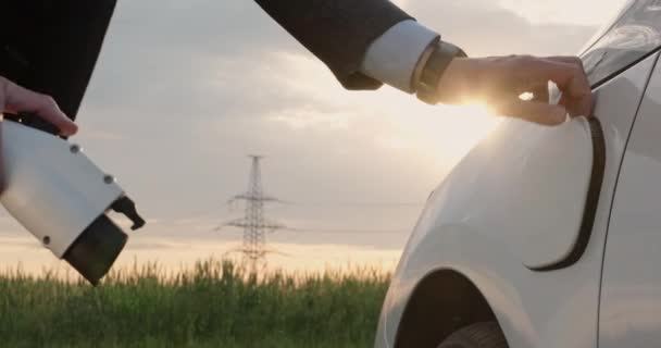 Empresário carrega eletomobile perto do campo com linhas de energia — Vídeo de Stock