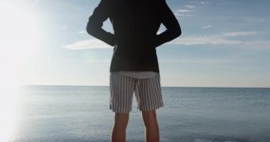 Çizgili şortlu bir adam iş ceketini ilikliyor, denize bakıyor, sırtından vurulmuş. Tatil için çok uzun süre bekledin, neredeyse tatildesin..