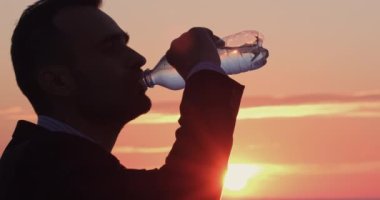 Şafak vakti bir şişeden su içerek susuzluğunu gideren siluetli bir adamın portresi. Su, gezegenin en değerli mineralidir..