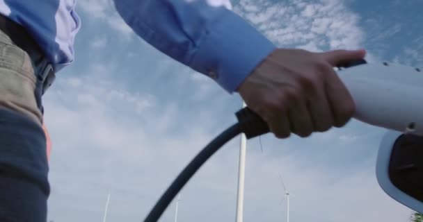 Řidič Připojí Nabíječku Svému Elektromobilu Větrnou Turbínou Pozadí Pomocí Obnovitelné — Stock video
