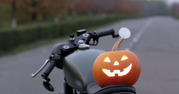 ヘルメットを被ったバイカーが バイクのシートから輝くハロウィーンのカボチャのランタンを拾い上げます すべての聖人の休日のバイカーとシンボル — ストック動画